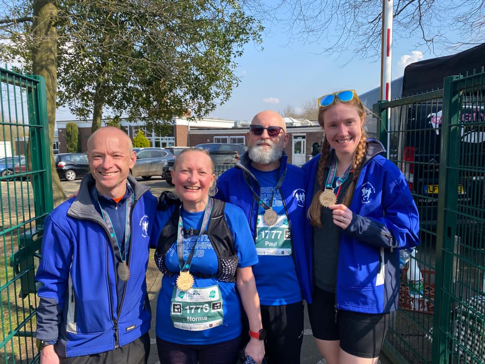 Four people stand at the end of a race, smiling and showing off their medals.